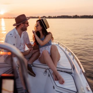 Beauitful young couple in love relaxing and having fun sailing to the sunset on a boat while on summer vacation