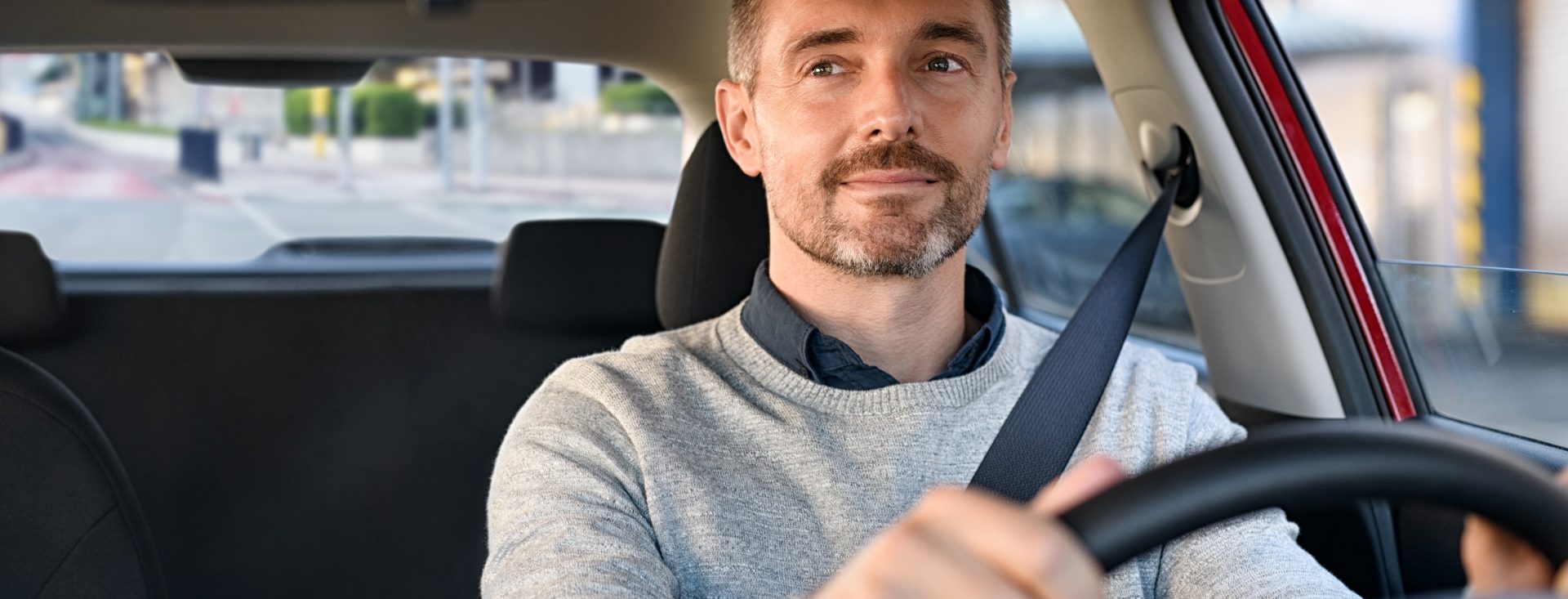 Mid adult casual man smiling while driving car and looking at mirror for reverse. Happy man feeling comfortable sitting on driver seat in his new car. Smiling mature businessman with seat belt on driving vehicle for transport and copy space.