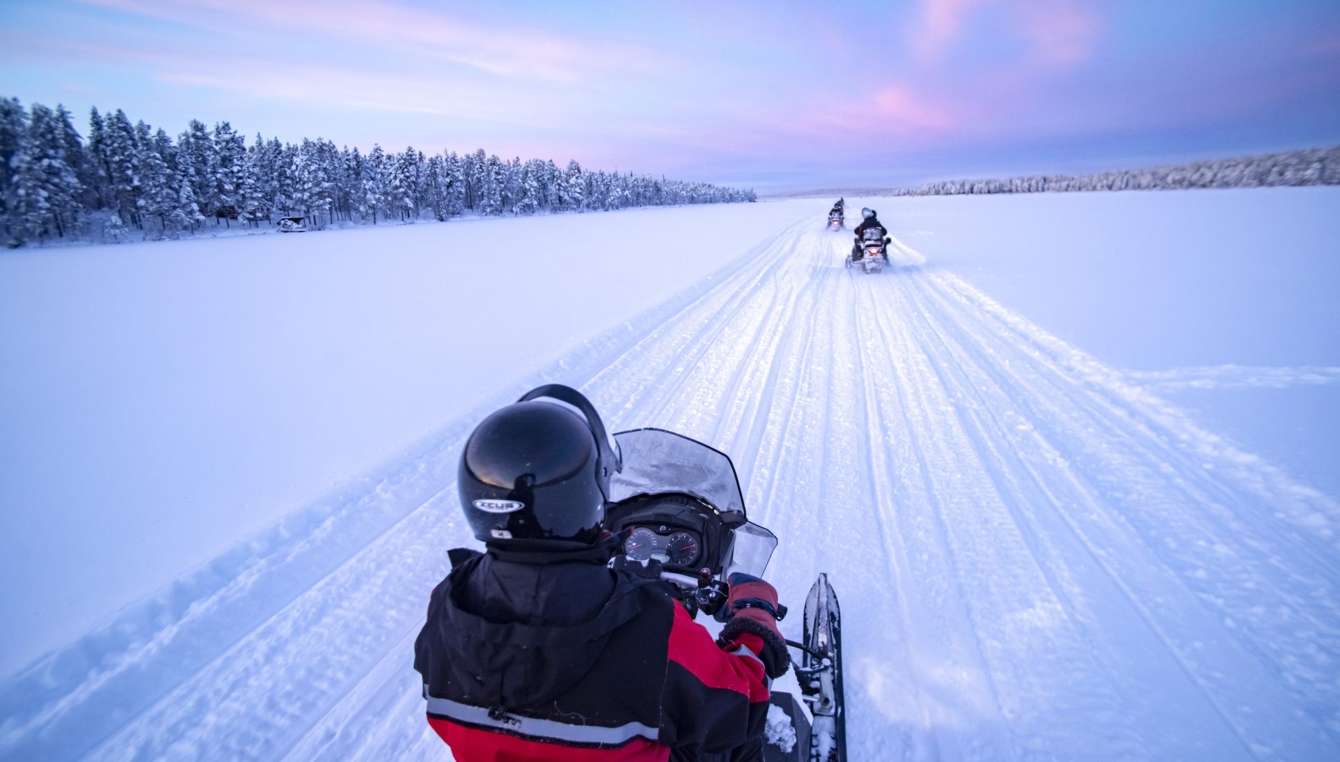 Snowmobiling on the frozen lake at sunset at Torassieppi, Lapland, Finland